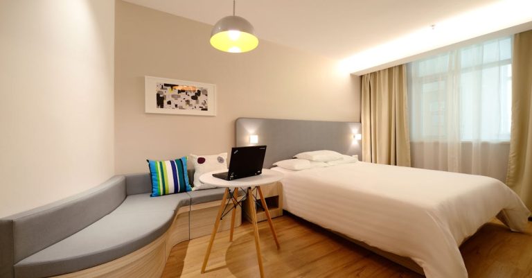 Modern hotel room featuring a bed, laptop, and stylish decor with ample lighting.